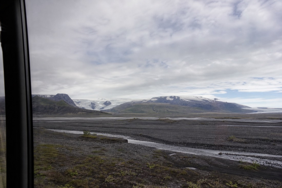 View from a coach window of Iceland's south coast, black sand plains and distant glacier tongues under a wide sky