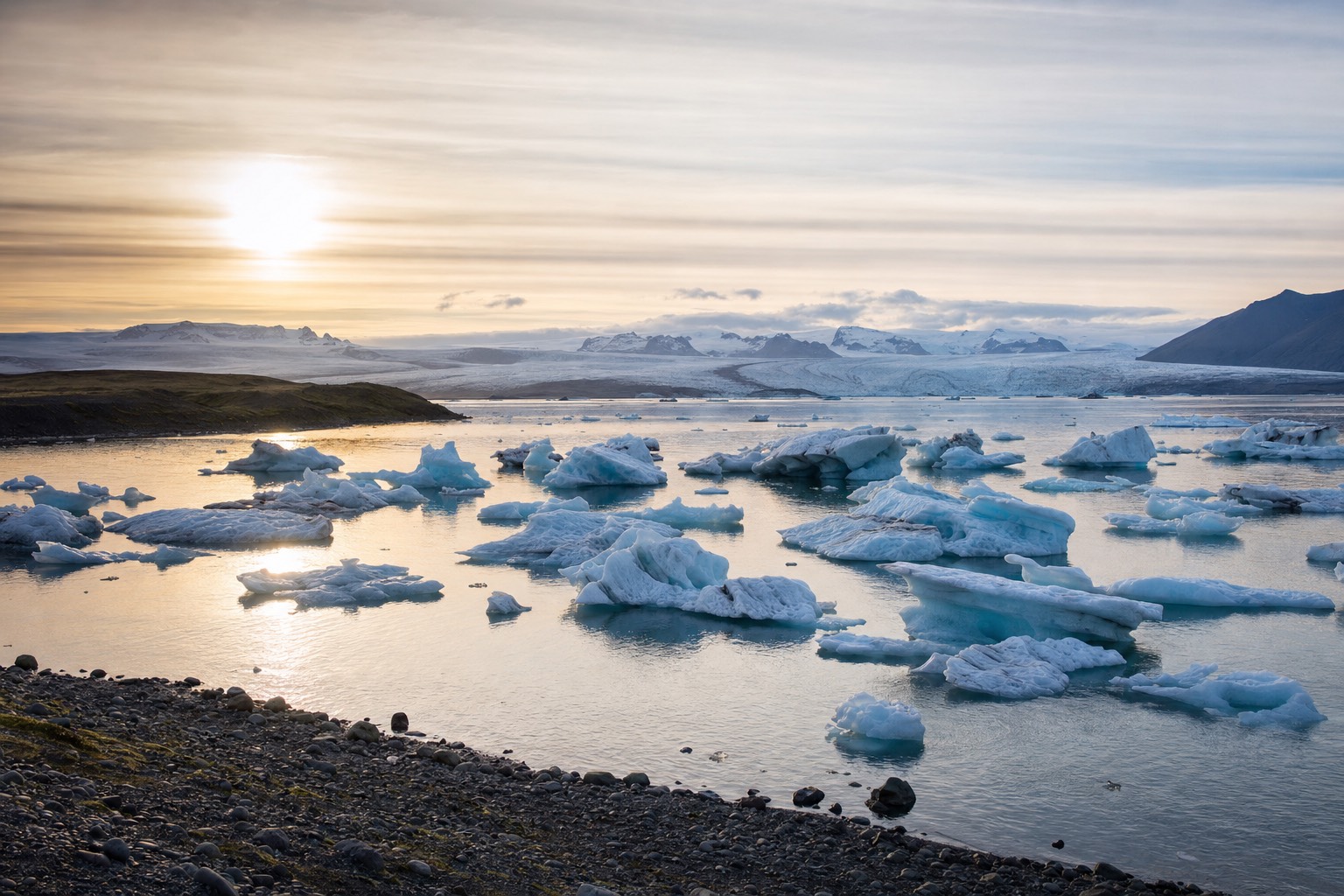 Jökulsárlón glacier lagoon with floating icebergs under a low golden sun, the tone shifting from summer green to winter blue