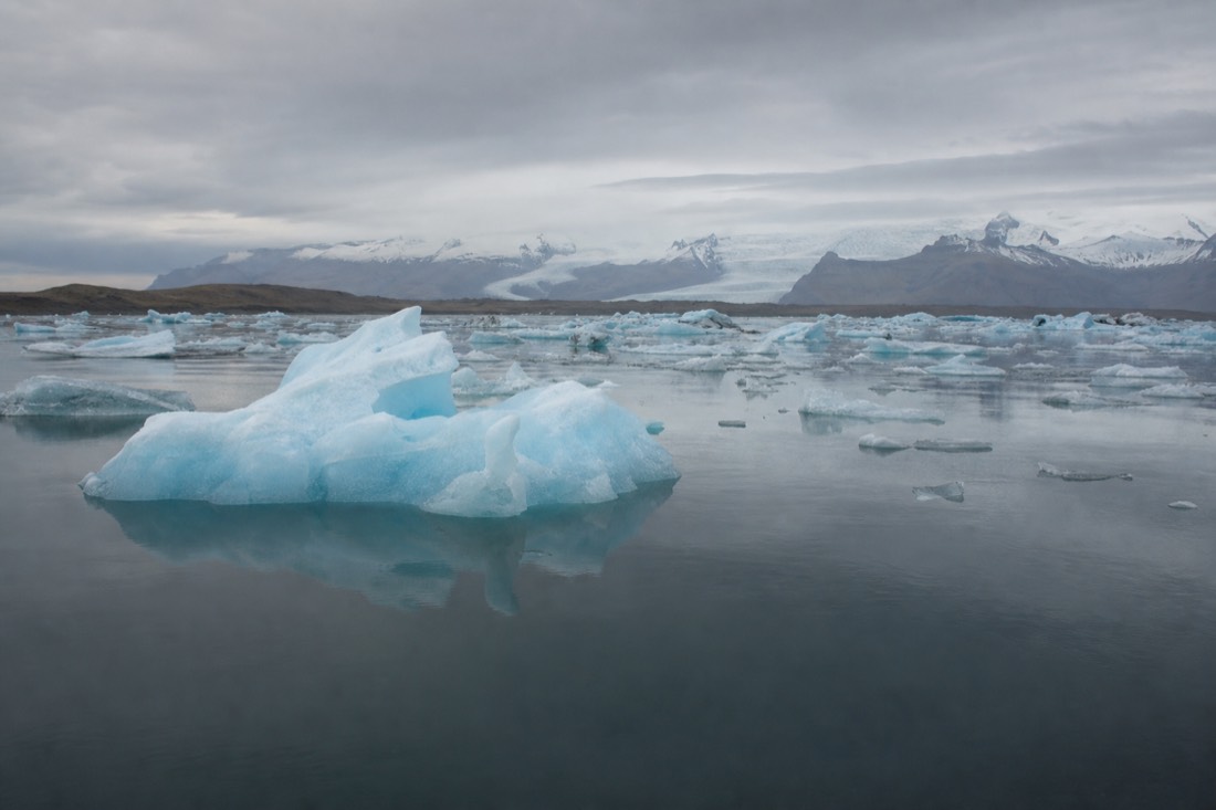 Blue-white icebergs drifting on the still surface of Jökulsárlón glacier lagoon under a low grey sky