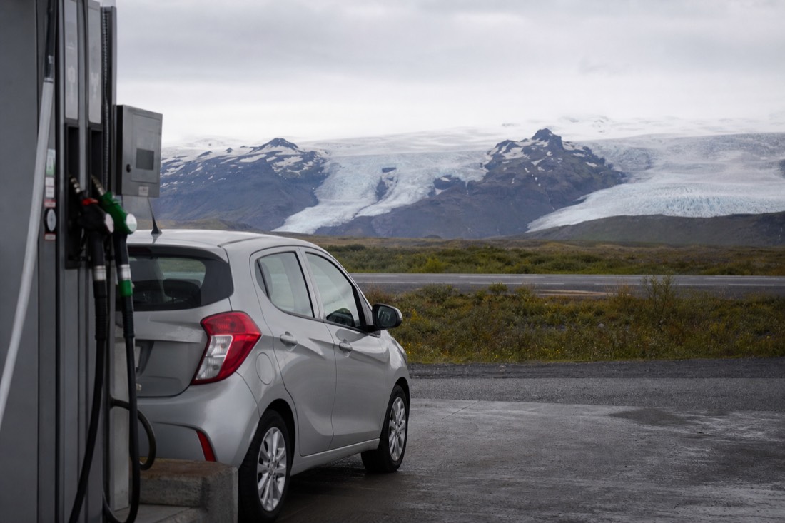 A small rental car at a fuel pump on Route 1 with Vatnajökull's glacier tongues in the distance on the drive to Jökulsárlón